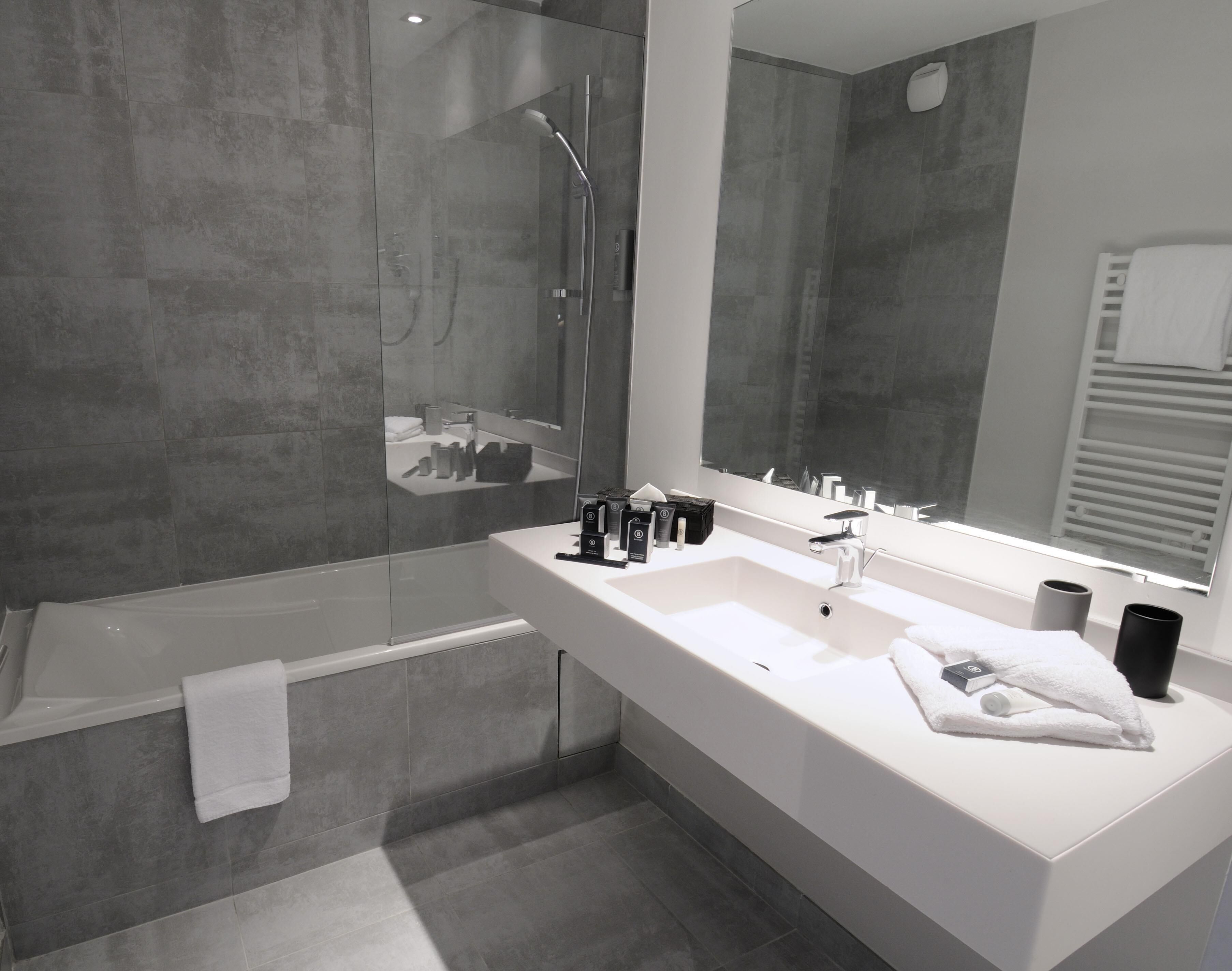 A modern bathroom with a glass-enclosed shower, a white sink with a large mirror, and a towel rack.