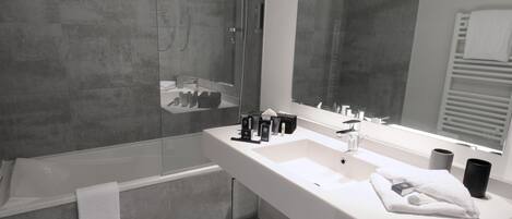 A modern bathroom with a glass-enclosed shower, a white sink with a large mirror, and a towel rack.