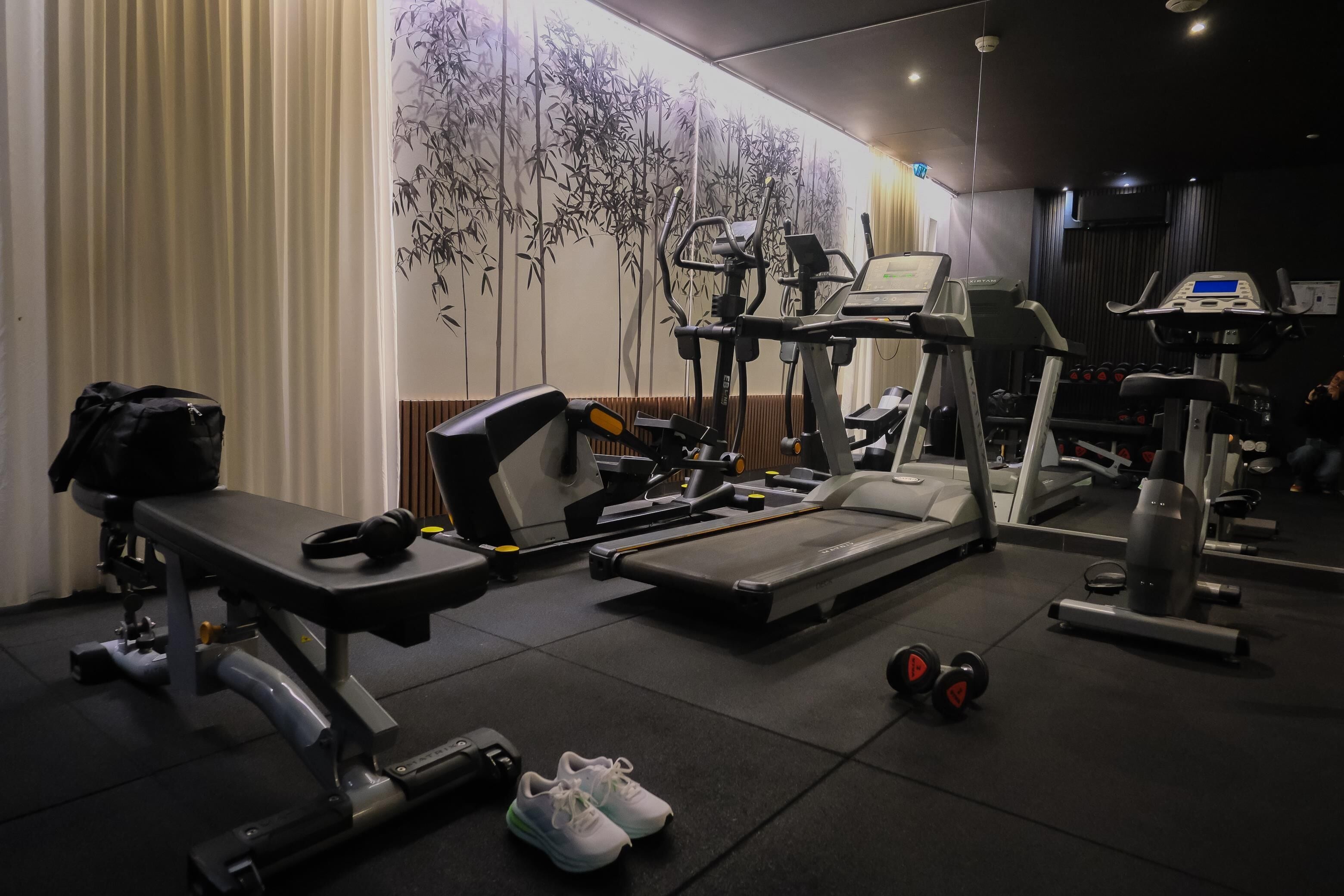 A gym with exercise equipment, a bench, dumbbells, and a wall with a bamboo design.