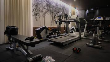 A gym with exercise equipment, a bench, dumbbells, and a wall with a bamboo design.