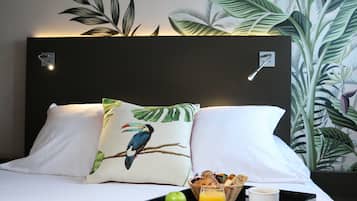 A neatly made bed with white linens, a pillow with a bird design, a tray with a green apple, a glass of orange juice, and a basket of pastries.