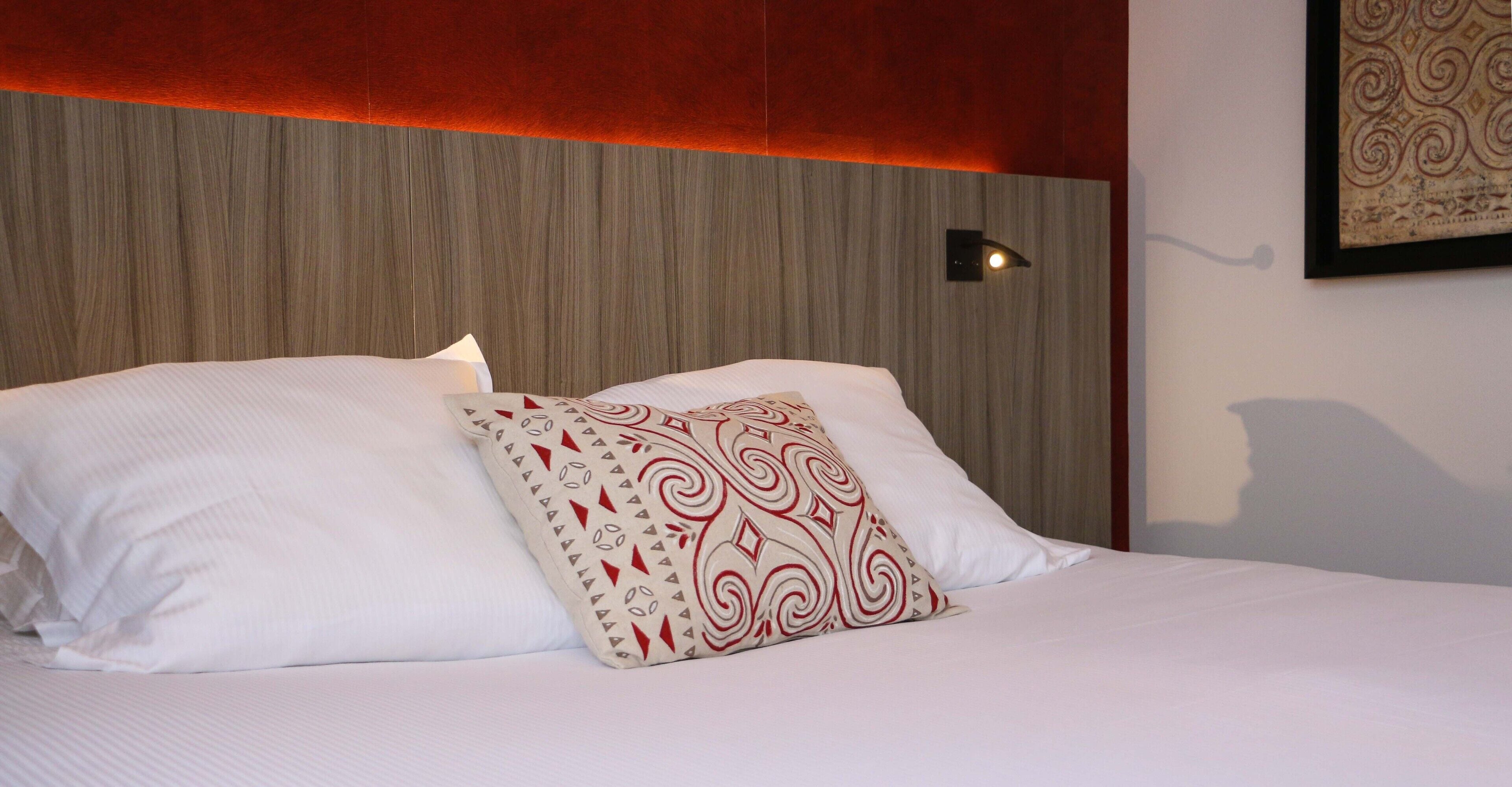 Een net opgemaakt bed met witte lakens en een decoratief kussen.