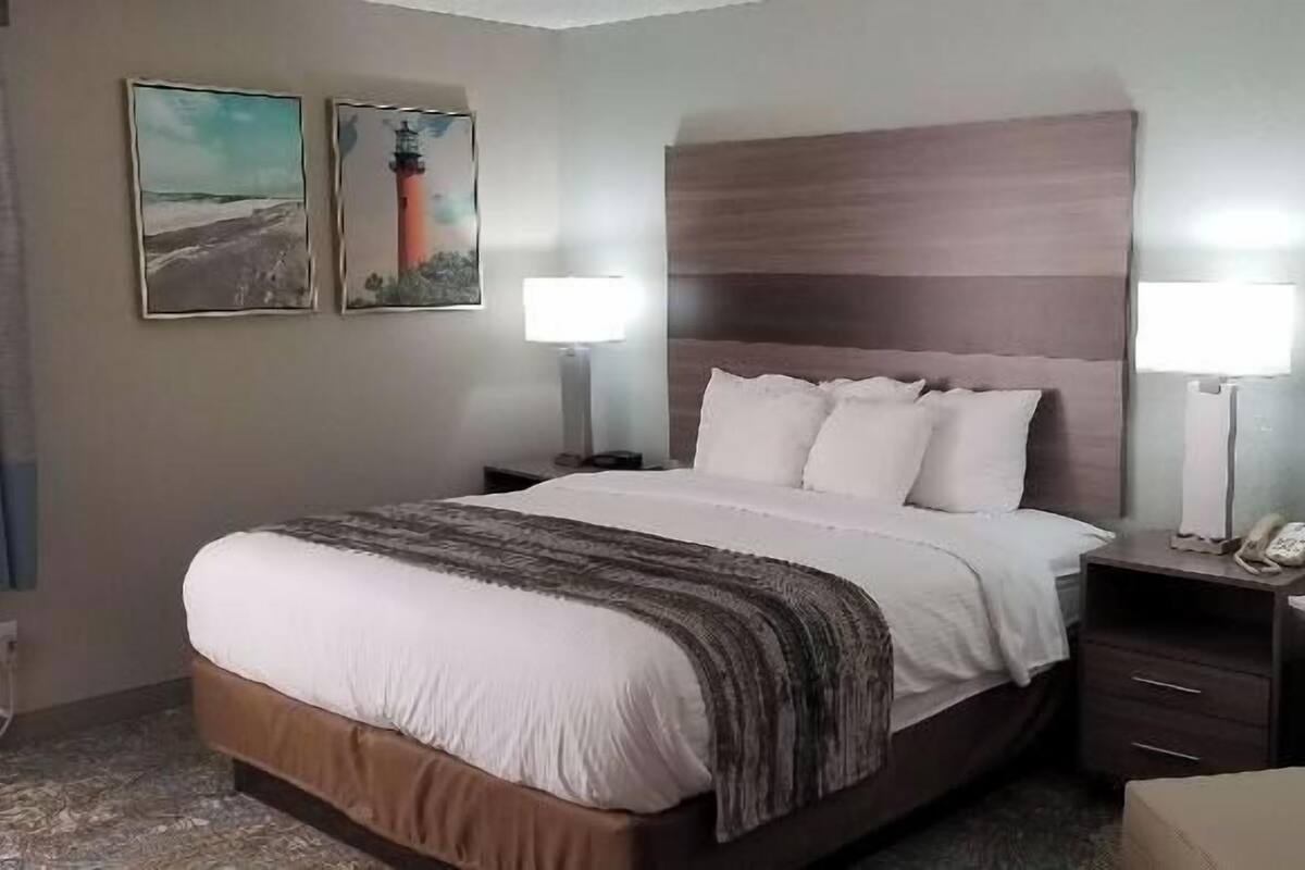 A hotel room with a bed, two bedside lamps, a chair, a nightstand, and two framed pictures on the wall.