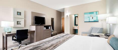 A hotel room with a bed, desk, chair, TV, and artwork on the walls.