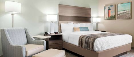 A hotel room with a large bed, a chair, a nightstand, and two wall-mounted lamps.