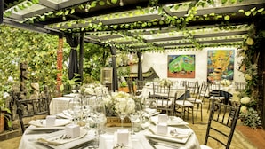 An outdoor dining area with tables set for a meal, surrounded by greenery and art.
