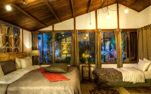 A bedroom with a large bed, a smaller bed, and a nightstand with a lamp. There are curtains on the windows, and a painting on the wall. - LA COLINA Hotel Cottage (Bogotá)