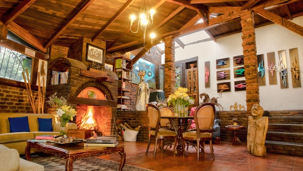 A cozy living room with a fireplace, wooden beams, and a dining area with chairs and a table.