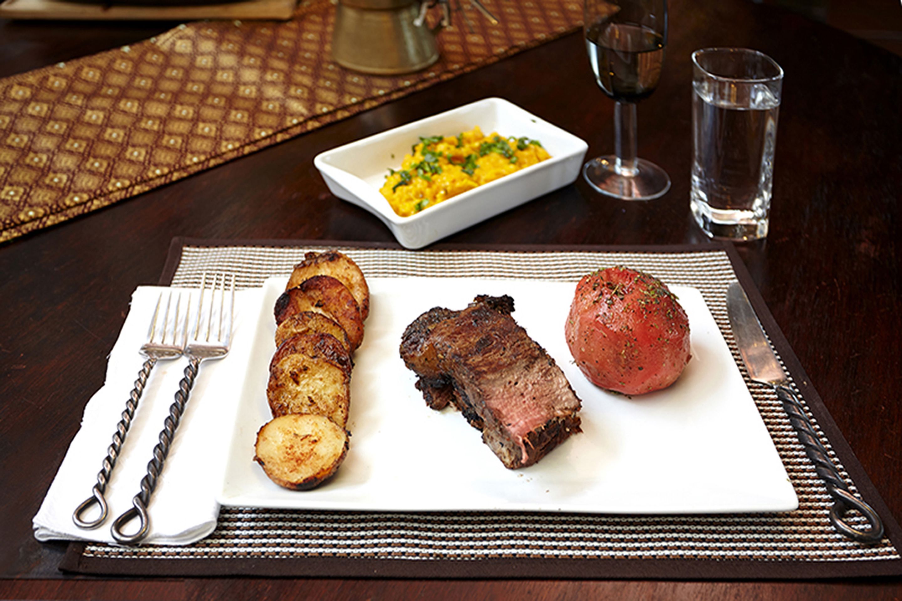 Une assiette contenant un steak et des pommes de terre, un verre d’eau et un verre à vin, le tout posé sur une table.