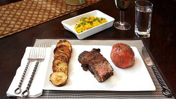 Une assiette contenant un steak et des pommes de terre, un verre d’eau et un verre à vin, le tout posé sur une table.