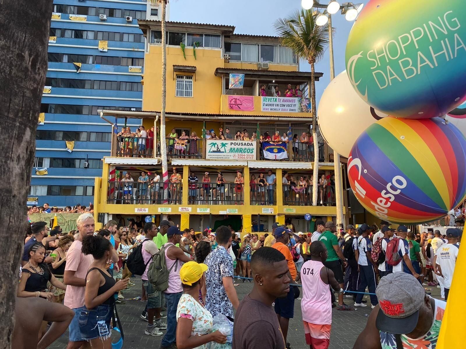 A crowded outdoor event with a building featuring balconies and banners.