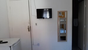 Una habitación con una puerta blanca, un pequeño electrodoméstico blanco, un televisor montado y una estantería de madera.