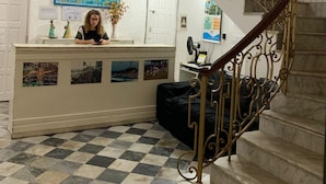Un vestíbulo con piso a cuadros, una recepción, una escalera con barandilla de metal decorada y un adorno de pared azul con estampado.