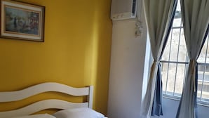 Habitación de hotel con cama, un cuadro en la pared, unidad de aire acondicionado y ventana con cortinas.