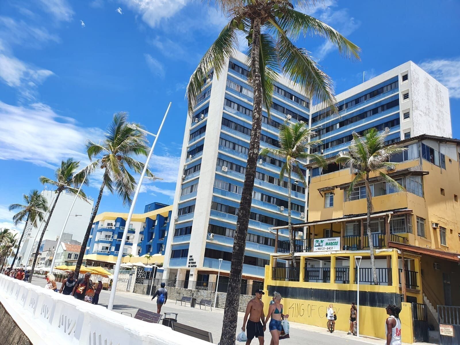 A multi-story hotel with balconies, palm trees, and a clear blue sky.