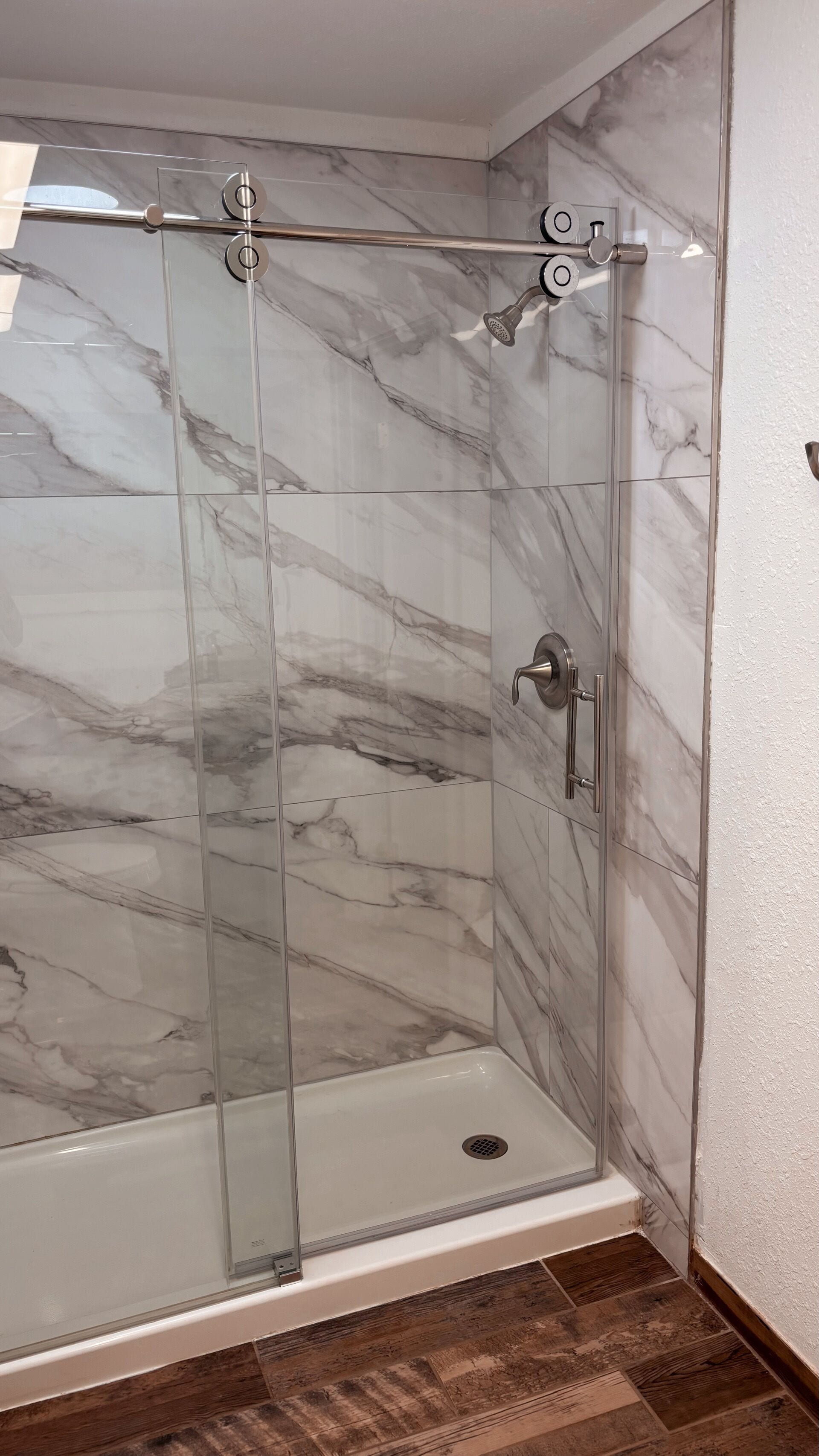 Une douche entièrementClose avec des parois en verre et un mur de fond en marbre.