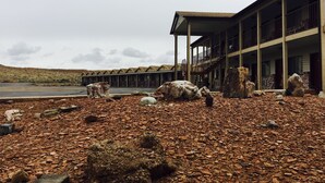 A building with a covered outdoor area, large rocks, and a barren landscape. - Whispering Sands Motel (Hanksville)