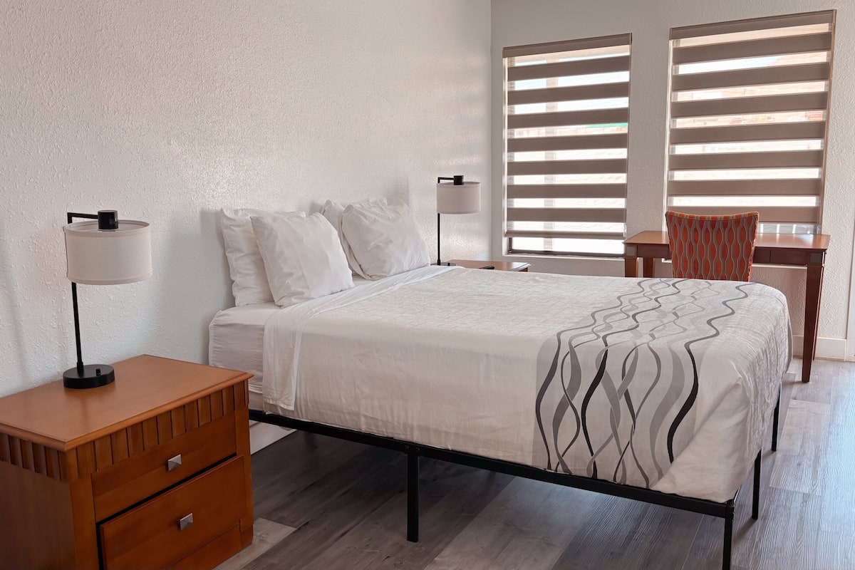A bedroom with a bed, bedside tables, a chair, and a window with blinds.