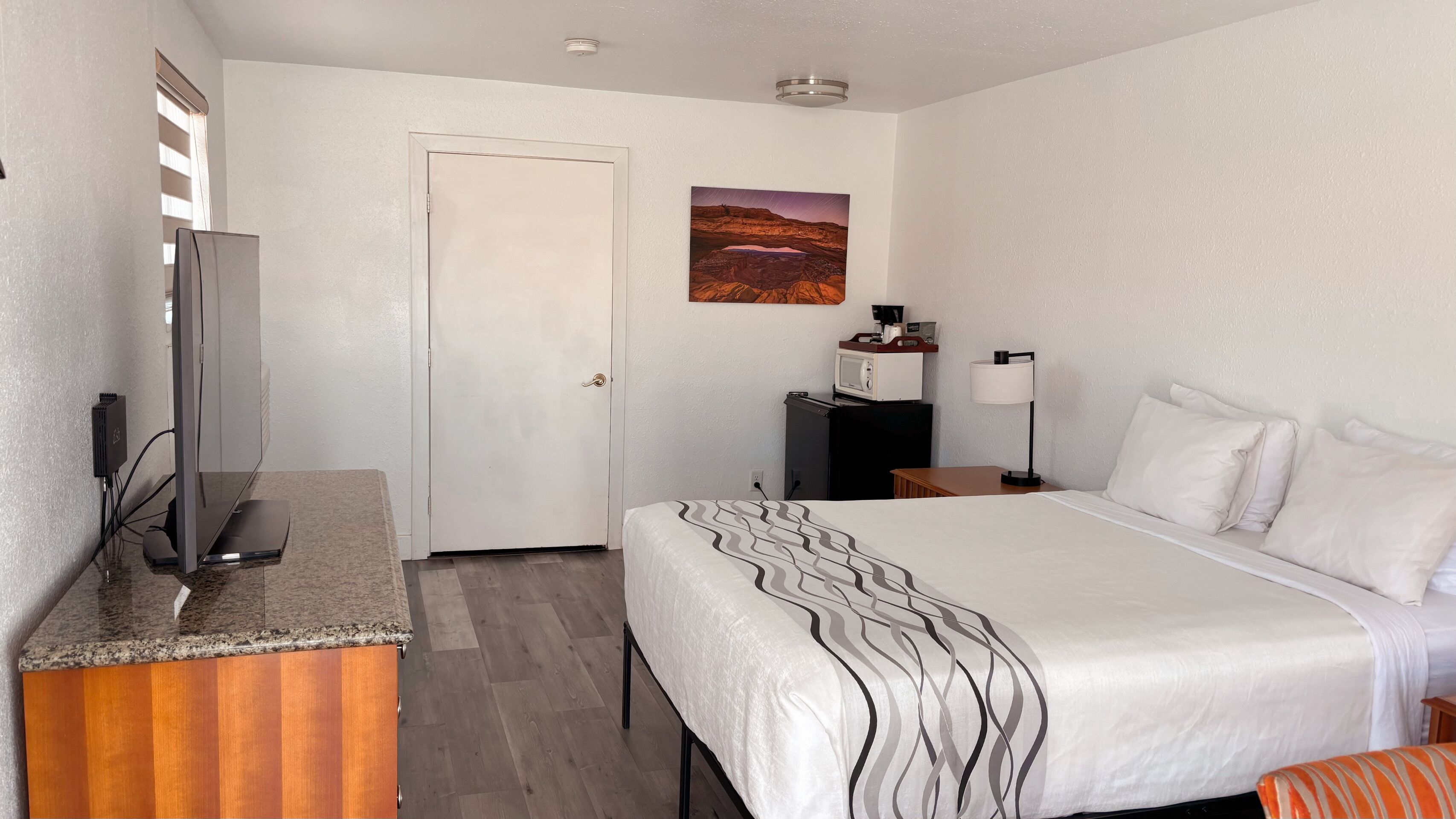 Een hotelkamer met een bed, een bureau, een televisie en een schilderij aan de muur.