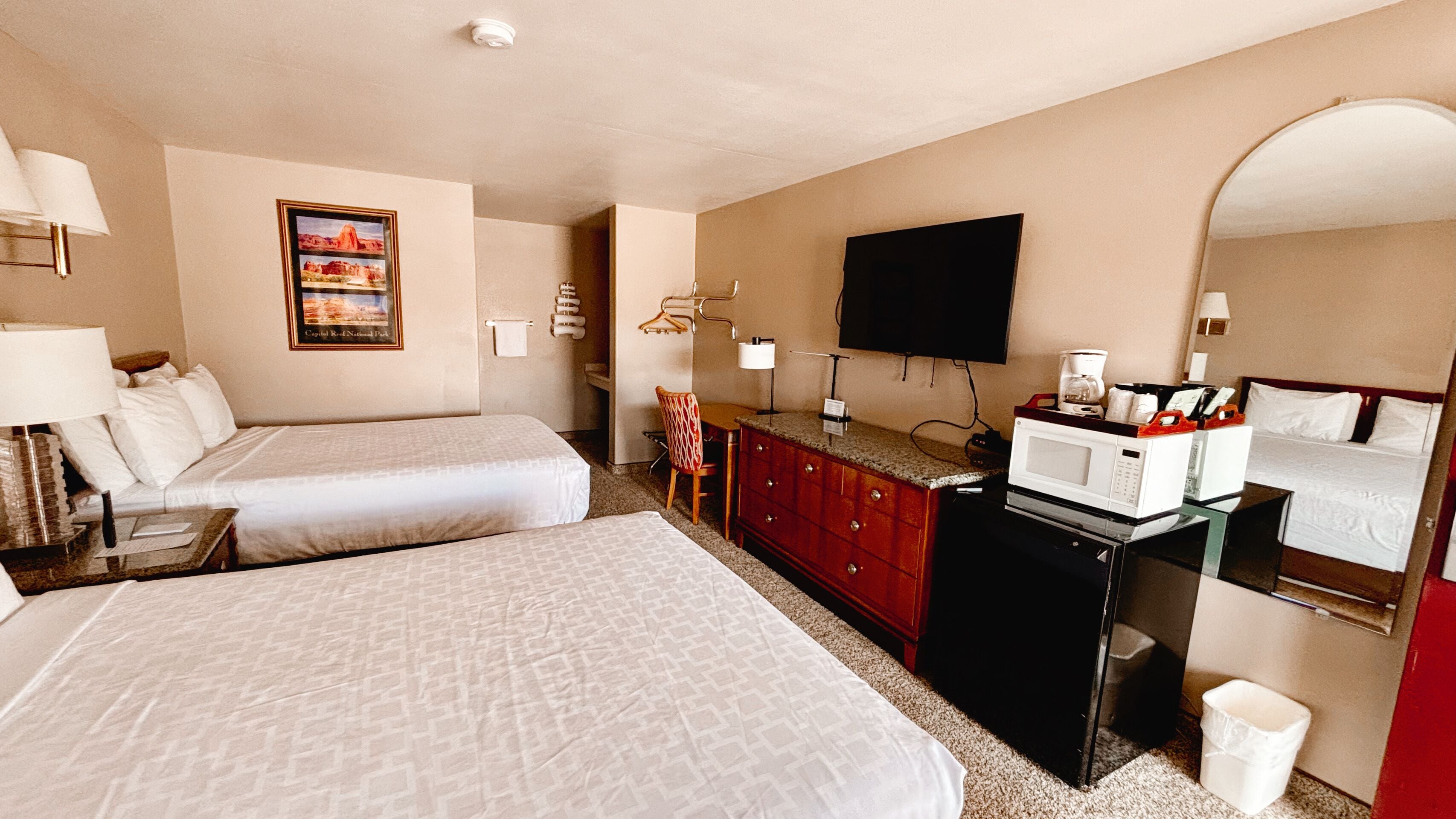 Habitación de hotel con dos camas, un escritorio con microondas, televisión y un cuadro en la pared.