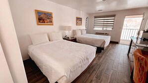 A hotel room with two beds, a desk, a chair, a window with blinds, and two framed pictures on the wall. - Whispering Sands Motel (Hanksville)
