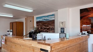 A reception desk with a wooden finish, a framed certificate, and a landscape painting on the wall. - Whispering Sands Motel (Hanksville)