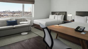 A hotel room with a bed, a desk, a chair, a sofa, and a city view.