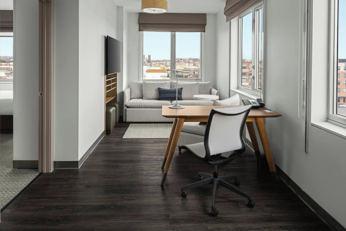 Un espacio de oficina moderno con un escritorio, una silla de oficina y un sofá. Hay un ventanal con vistas a la ciudad.