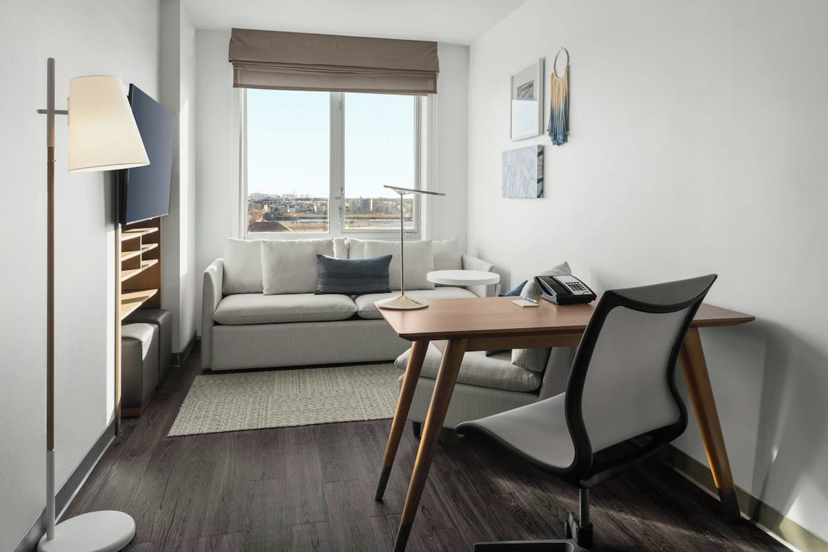 Una habitación moderna con sofá, escritorio, silla, lámpara y ventana con vista a la ciudad.