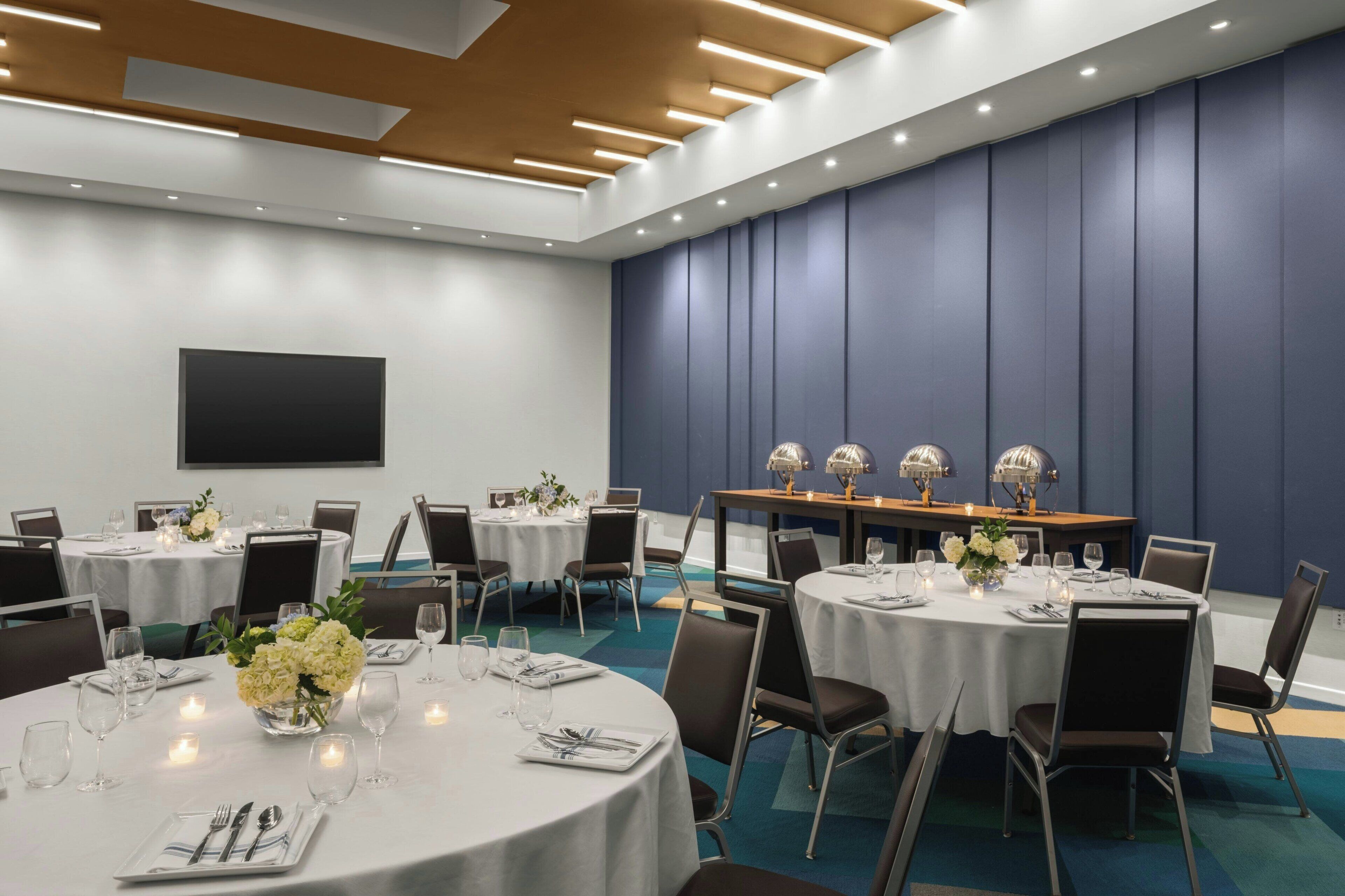 A conference room with round tables, chairs, and a large screen.