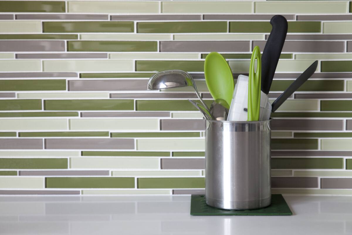 Un recipiente para utensilios de cocina con una cuchara, un cucharón y un cuchillo sobre un posavasos verde.