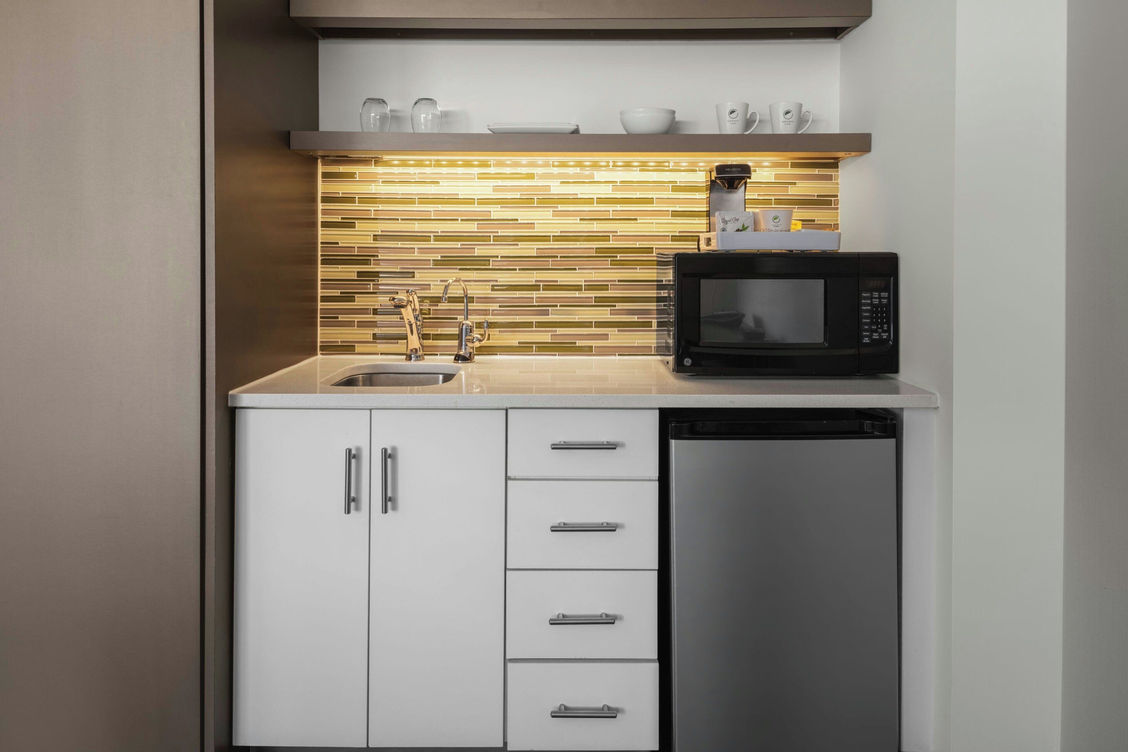 A compact kitchen with a microwave, dishwasher, and a tiled backsplash.