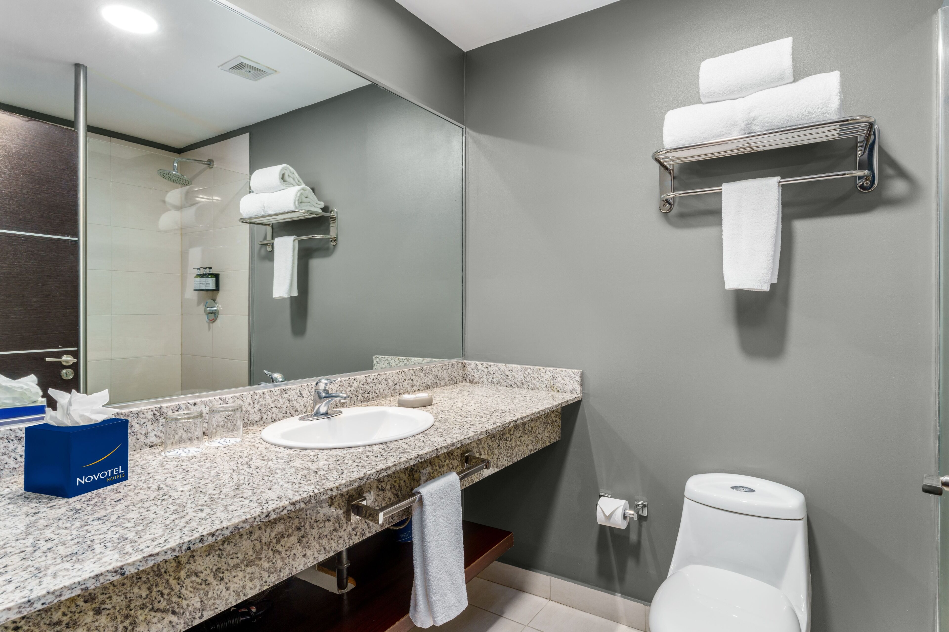 A modern bathroom with a granite countertop, a sink, a mirror, a towel rack, and a toilet.
