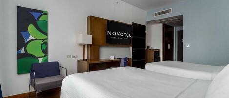 Una habitación de hotel con dos camas, un escritorio, una silla, un televisor y un cuadro en la pared.
