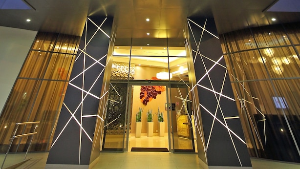 Een moderne hotelentree met een opvallend 'NOVOTEL'-bord, grote glasramen en geometrische lichtpatronen op de gevel.