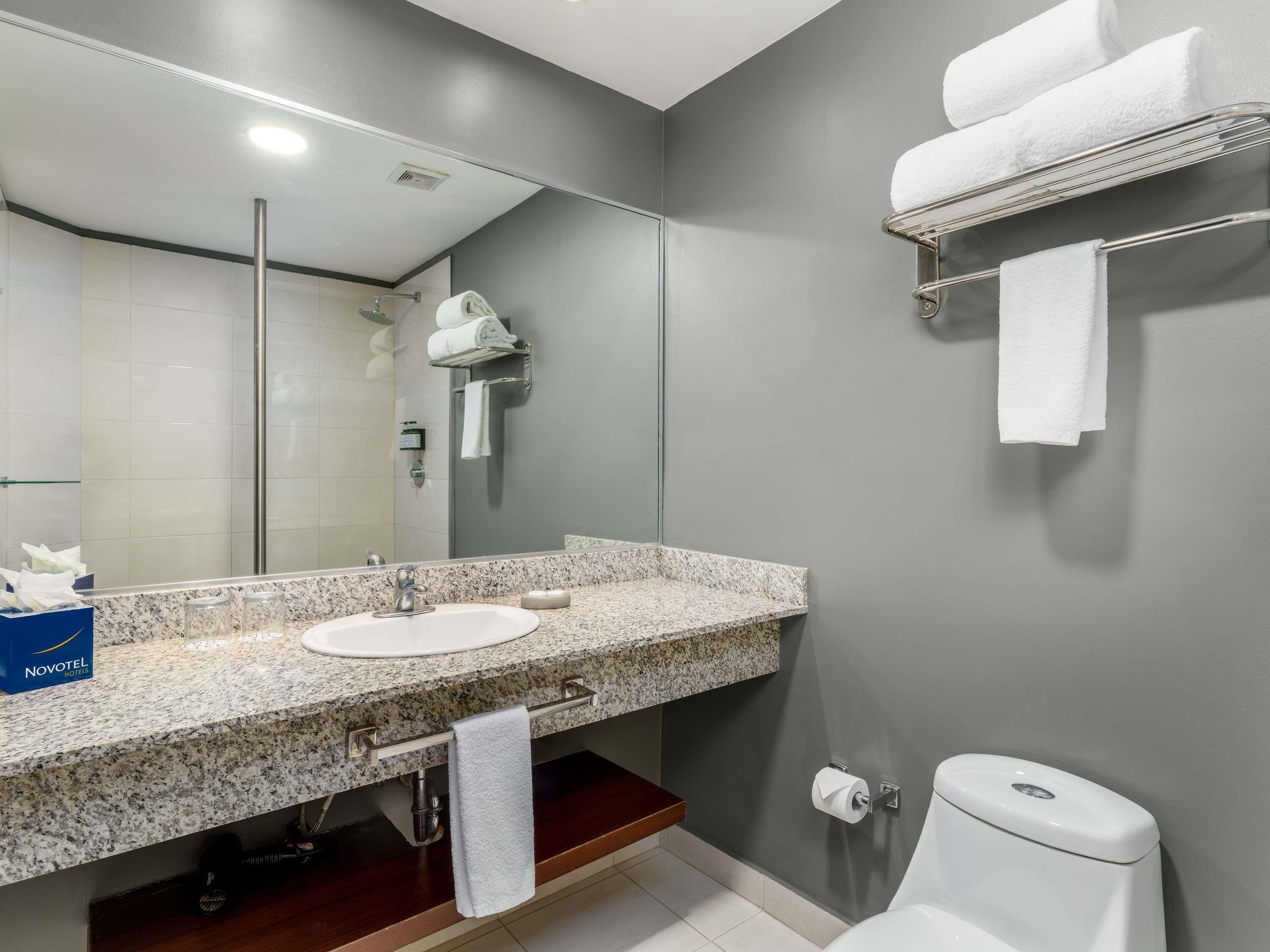 A modern bathroom with a granite countertop sink, a mirror, a towel rack, and a toilet.