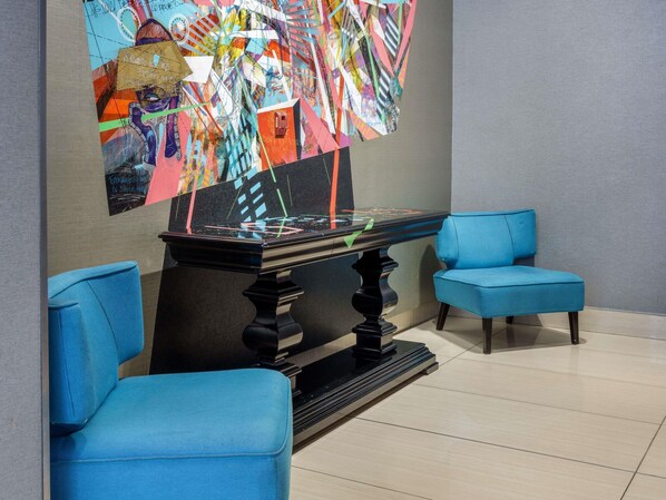 A room with a glass-top table, two blue chairs, and a colorful abstract wall art piece.