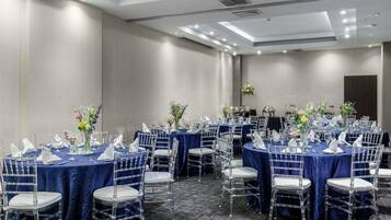A conference room with multiple tables, clear chairs, and blue tablecloths.