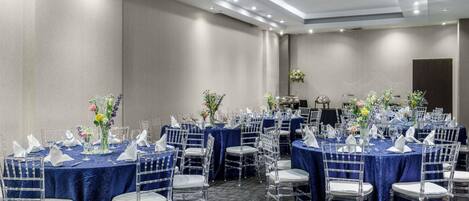 Un salón de conferencias con varias mesas, sillas transparentes y manteles azules.