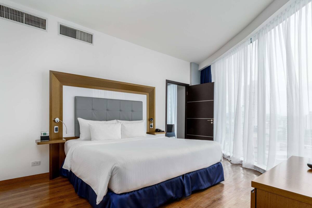 Une chambre d’hôtel comprenant un lit, des tables de chevet, une armoire et une fenêtre avec des rideaux.