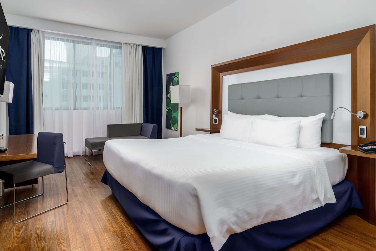 A hotel room with a large bed, a desk with a chair, a sofa, a TV, and a window with curtains.