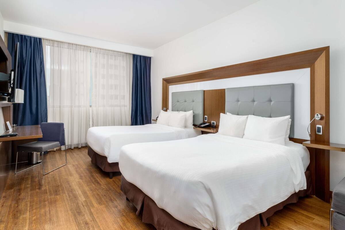 A hotel room with two beds, a desk, and a chair.