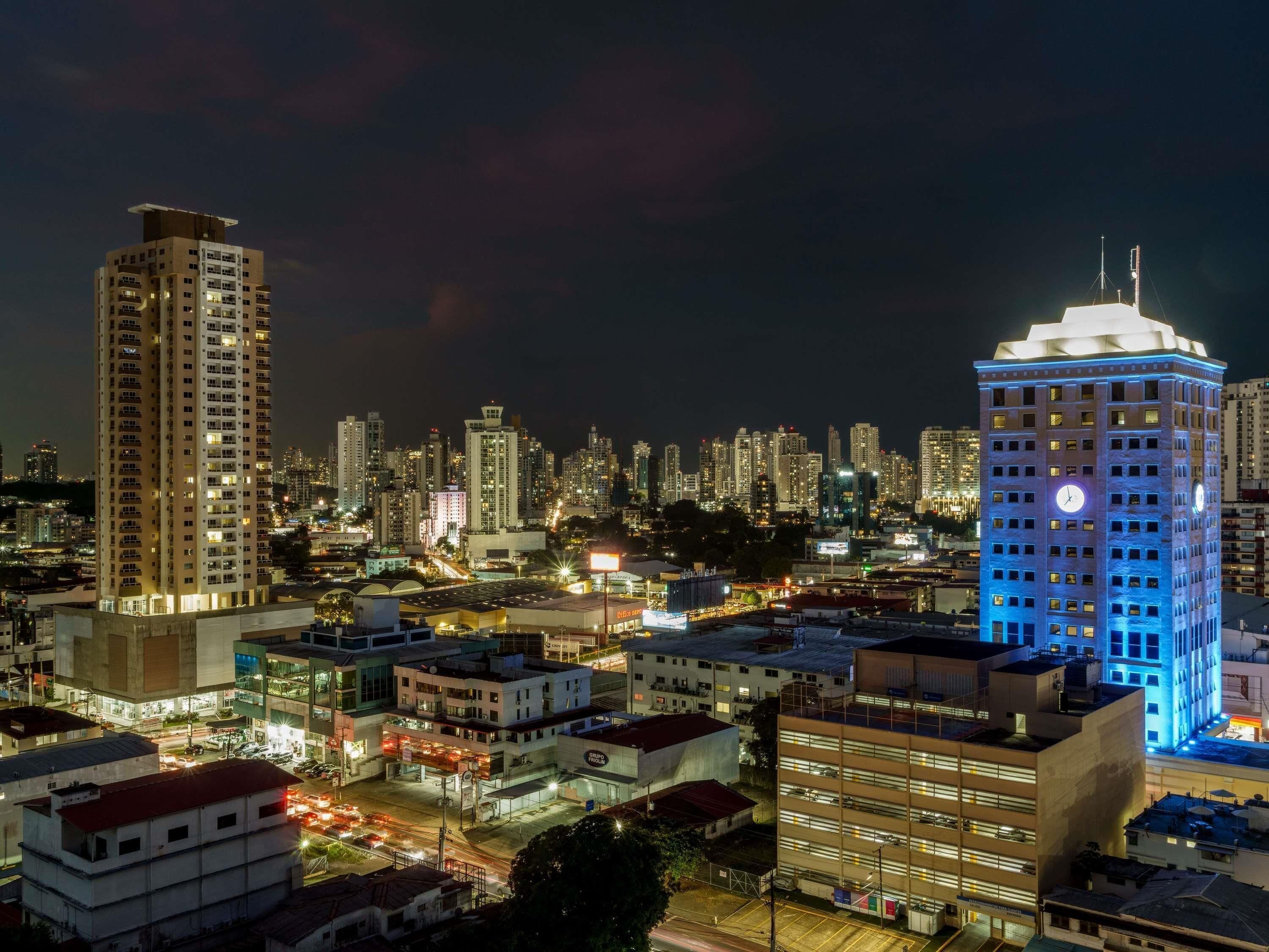 A high-rise building with a clock tower, surrounded by other tall buildings in a cityscape.