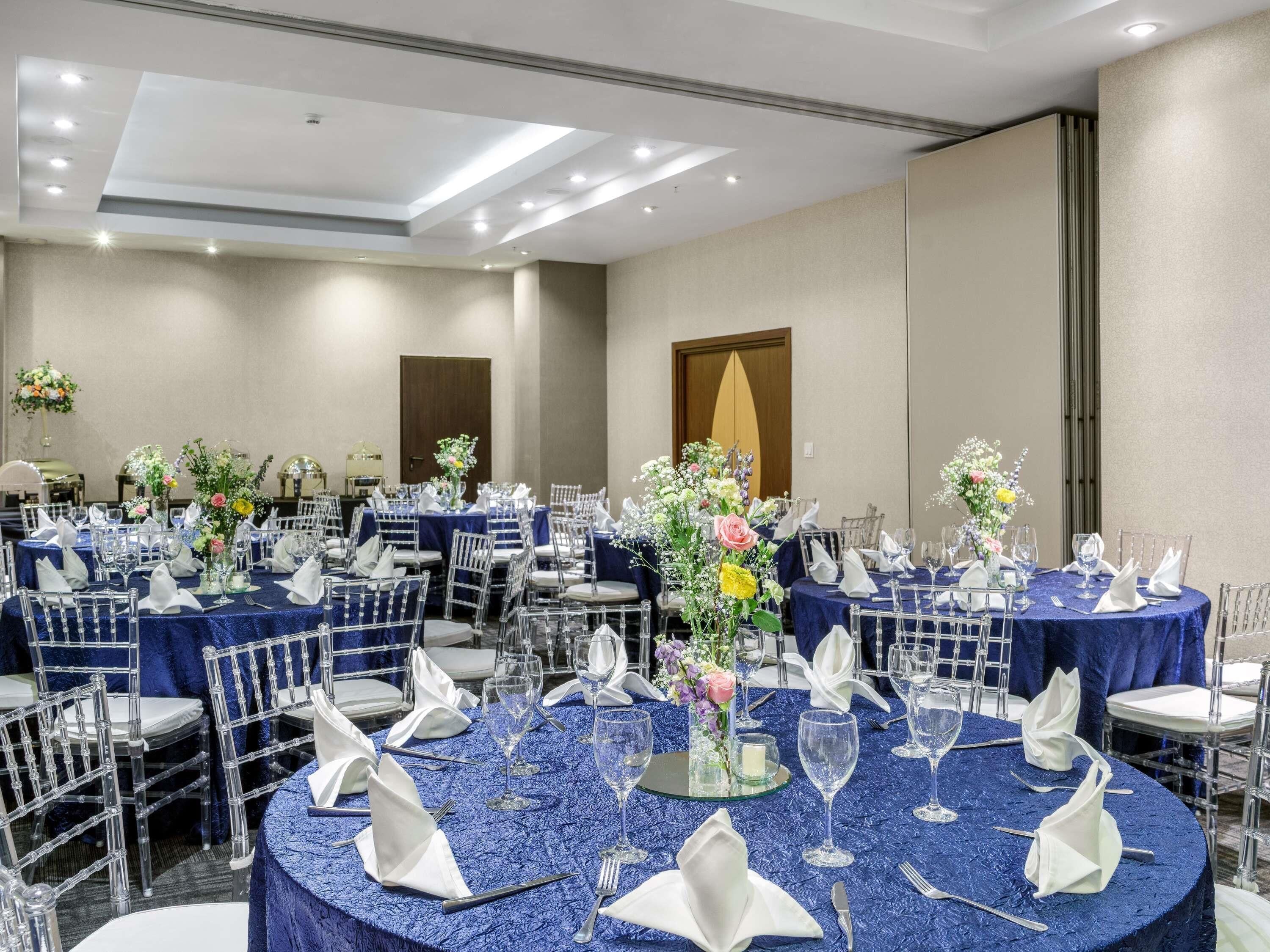 Un salón de banquetes con mesas redondas, sillas y centros de mesa florales.