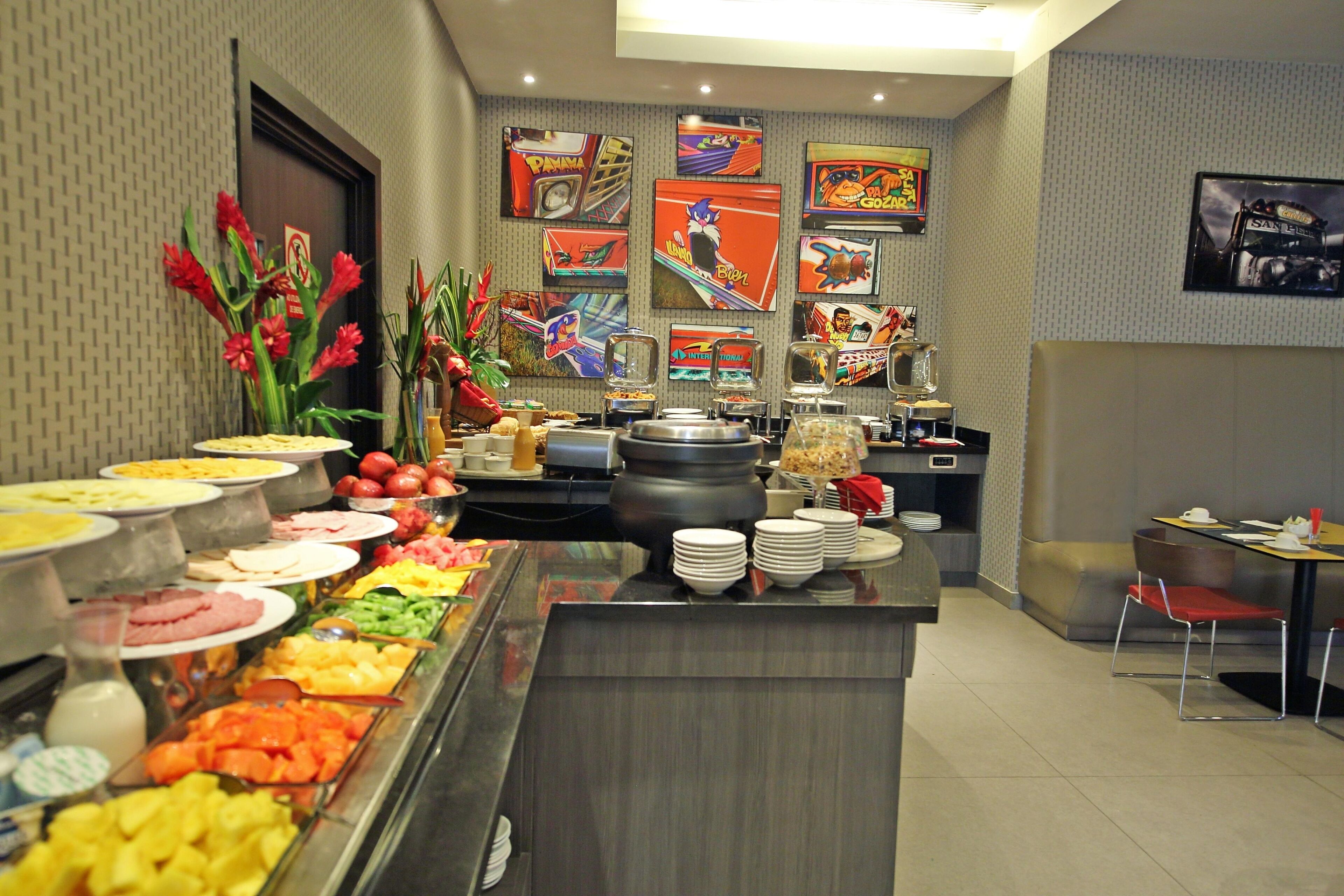 A buffet with various food options, a seating area with chairs, and a wall decorated with colorful artwork.