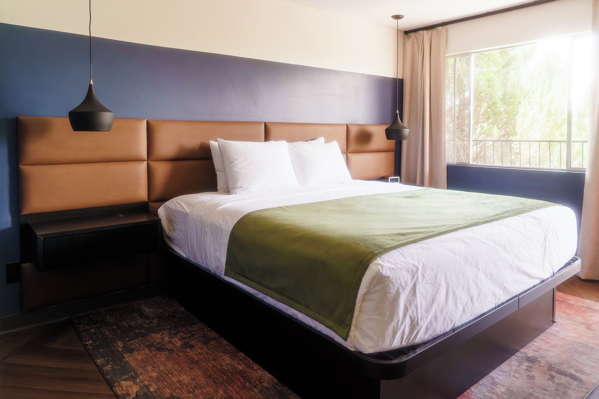 Une chambre d’hôtel avec un lit, une table de chevet, une lampe et une fenêtre avec des rideaux.