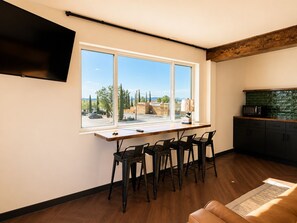 A modern kitchen with a large window, a dining area with chairs, and a flat-screen TV mounted on the wall. - The Wesley Hotel (Page)