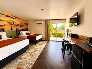 A hotel room with two beds, a desk, a television, and a view of the outdoors. - The Wesley Hotel (Page)