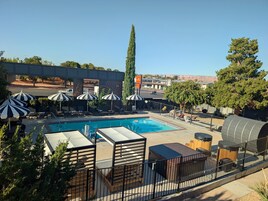 Zona de piscina con sillones reclinables y sombrillas, un árbol alto y vistas del paisaje circundante.