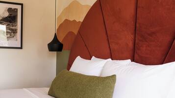 A bed with white bedding and a green pillow, a red headboard, a black pendant light, and a framed picture on the wall.